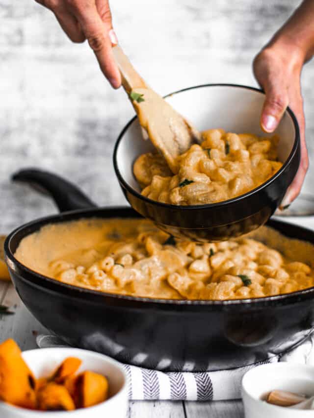 A person scooping macaroni and cheese out of a skillet.