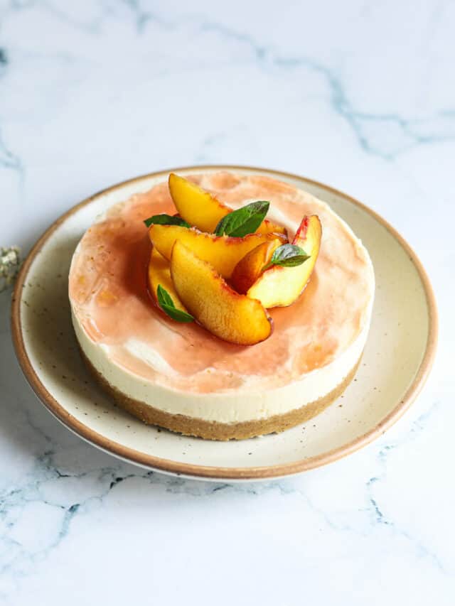 A peach cheesecake on a plate with mint leaves.