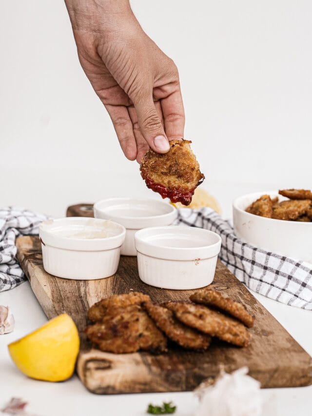 A person is dipping a fried chicken wing into a sauce with more wings and dips arranged on a wooden board.
