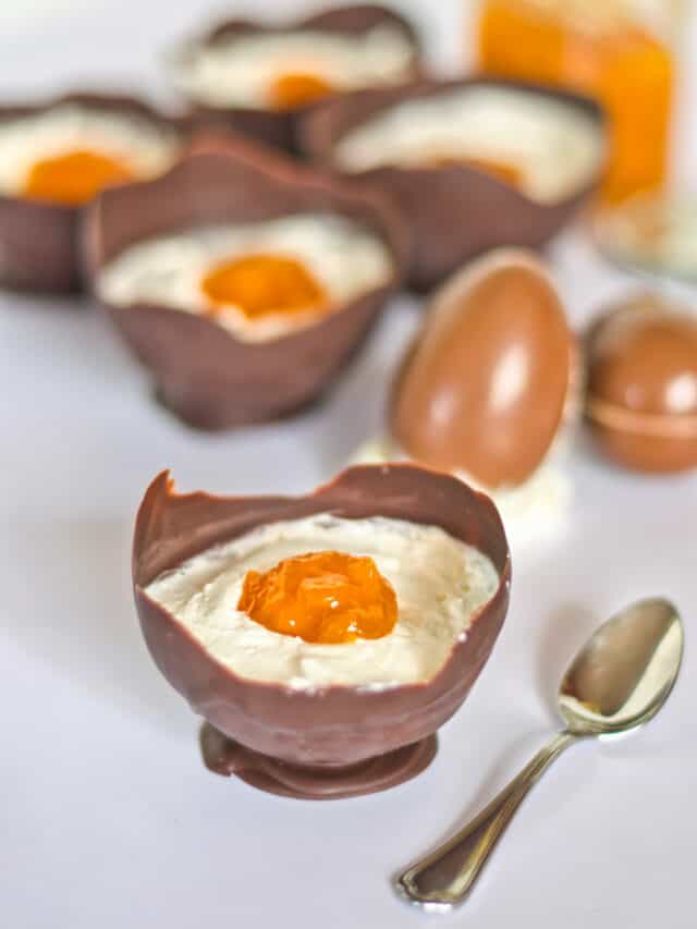 Chocolate eggs filled with a white and yellow dessert to resemble boiled eggs, with a spoon on the side.