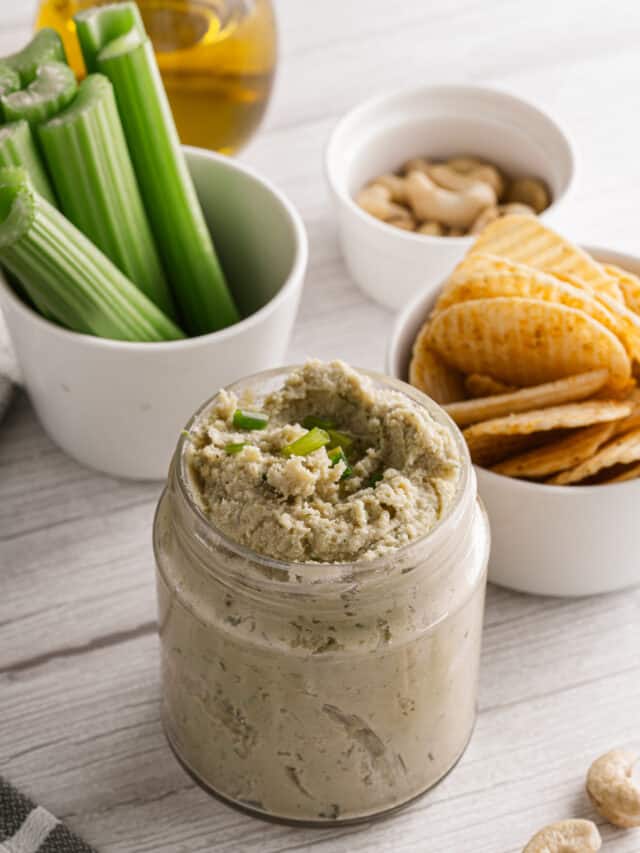 A jar of cashew hummus with celery and chips.
