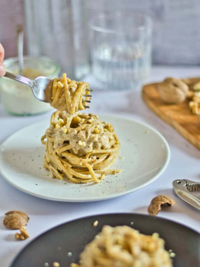 A person holding a fork over a plate of pasta.