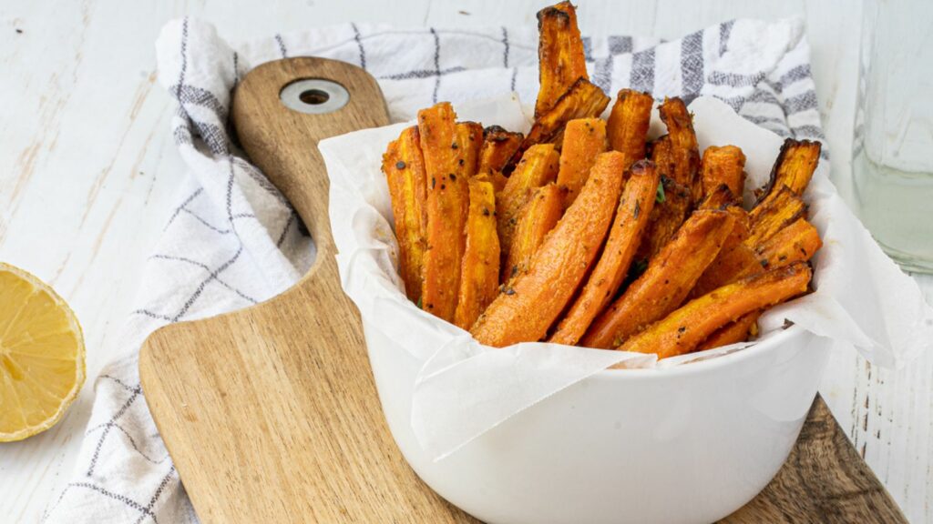 Carrot fries in a bowl on a wooden cutting board.