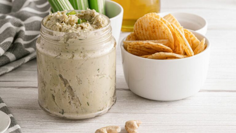 A jar of cashew dip with chips on a wooden table.
