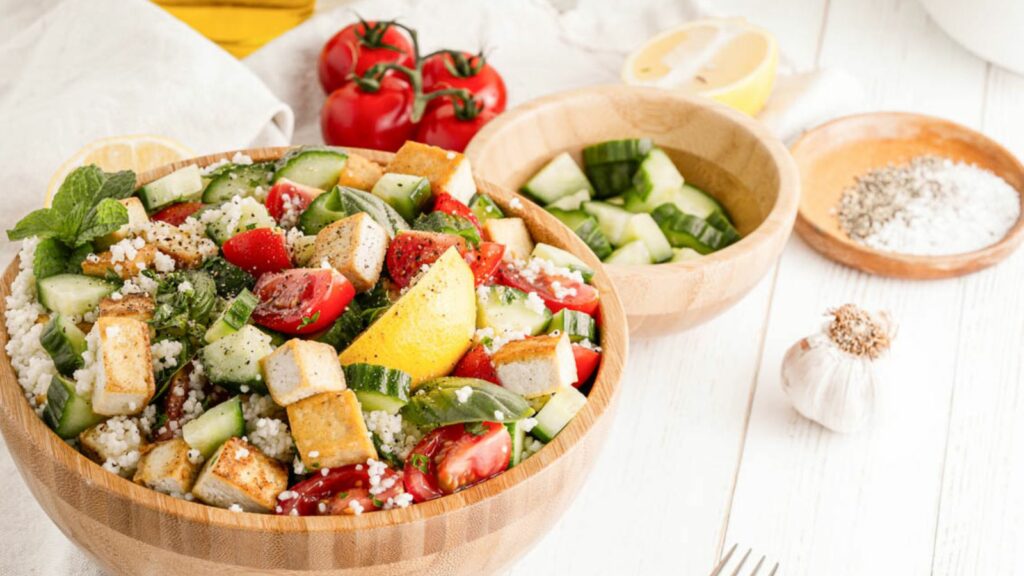 A bowl of tofu salad with tomatoes, cucumbers and lemons.
