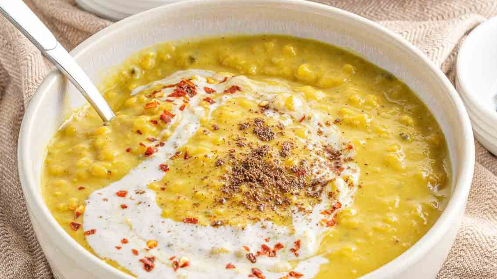 A bowl of yellow lentil dal with sour cream and a spoon.
