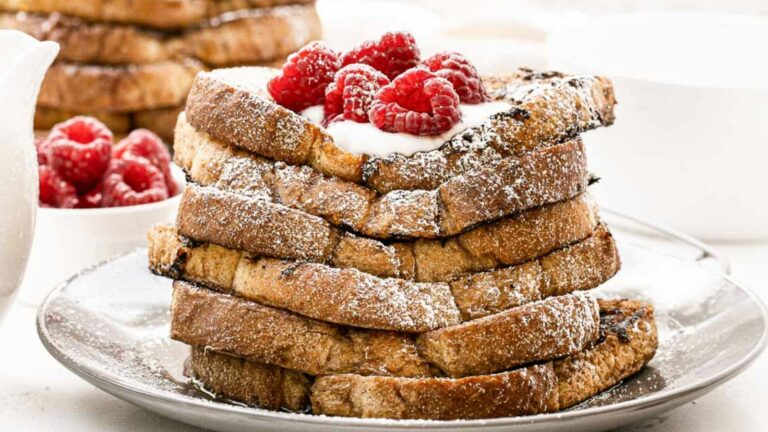 A stack of French toast with raspberries on a plate.