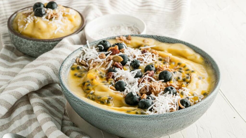 A bowl of mango smoothie with blueberries and nuts.