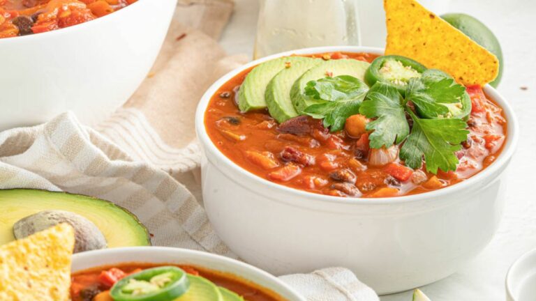 A bowl of chili with avocado, tortilla chips and guacamole.