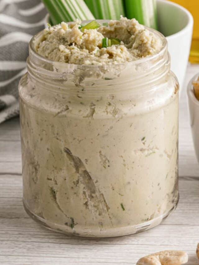 A jar of cashew dip with chips on a wooden table.