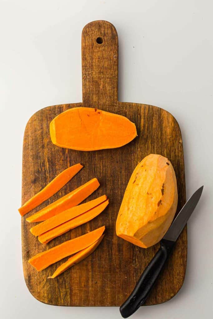Sweet potatoes with a  knife on a cutting board.