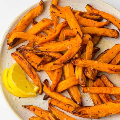 Sweet potato fries on a plate with lemon wedges.