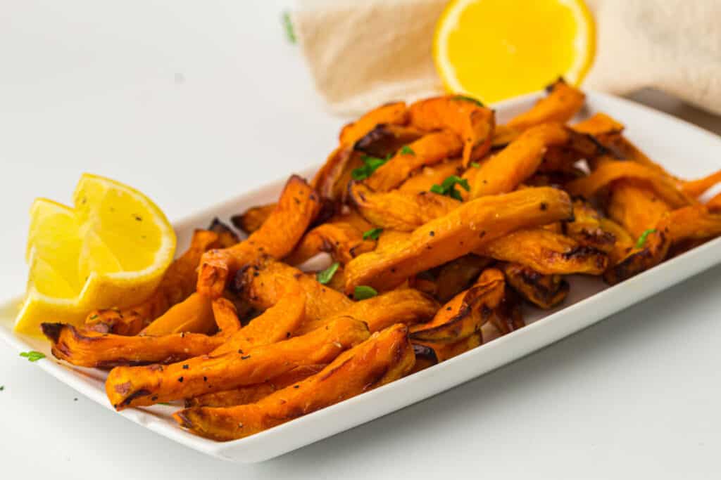 Air fried sweet potato fries on a white plate with lemon wedges.