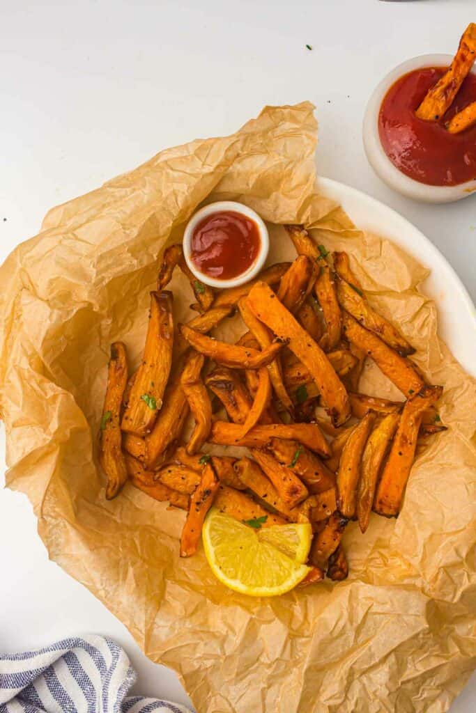 A plate of sweet potato fries with ketchup and lemon wedges.