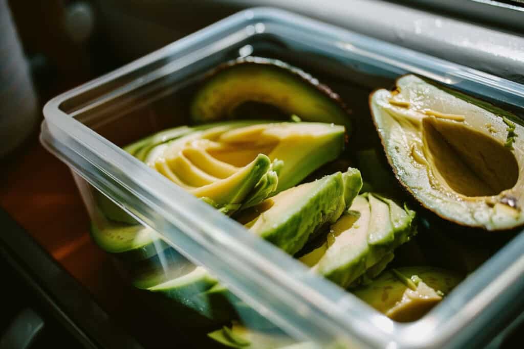 Sliced avocados in a plastic container on a plane.