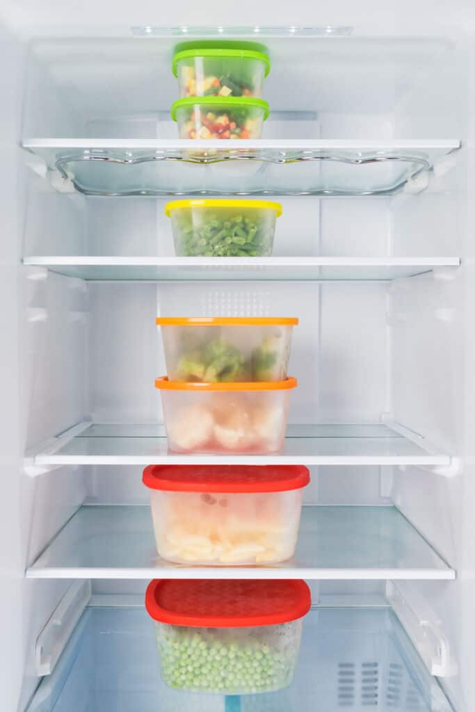 A refrigerator full of plastic containers filled with vegetables.