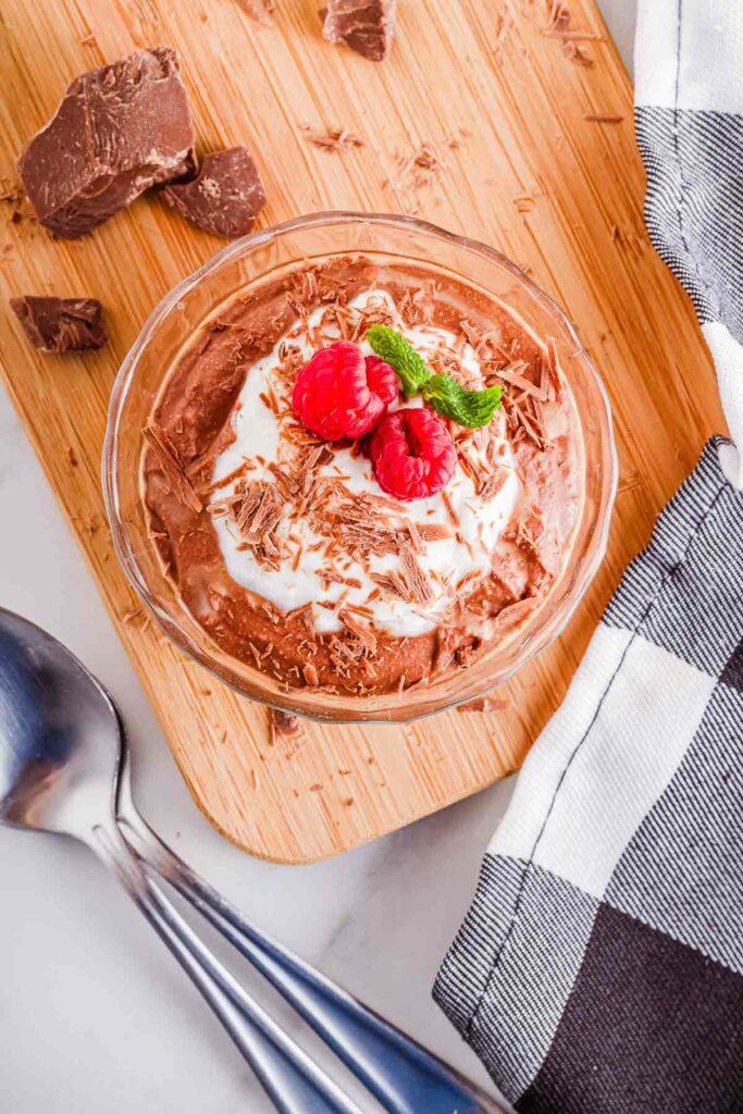 A bowl of chocolate coconut mousse with whipped cream and raspberries.