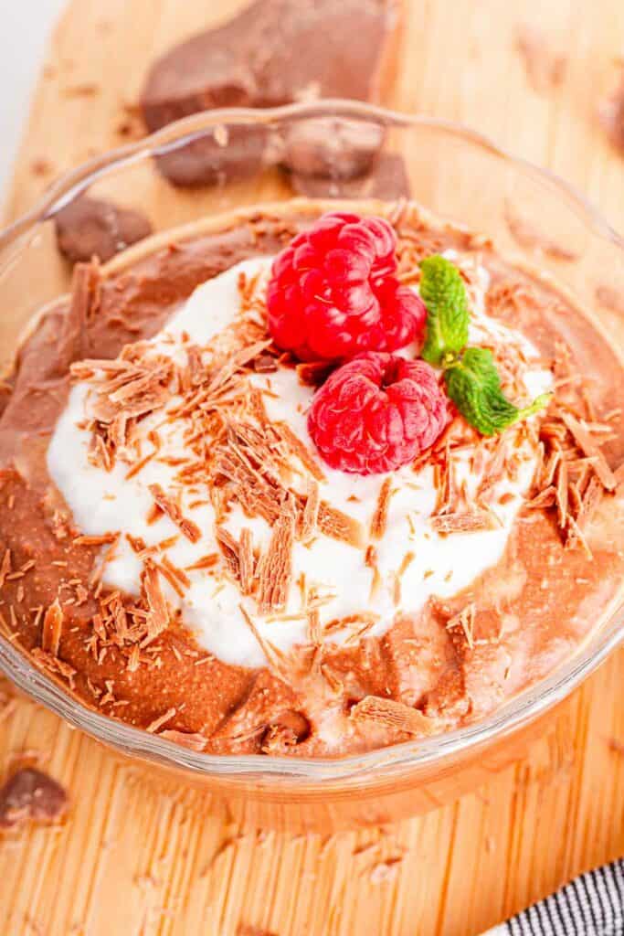 A bowl of chocolate coconut mousse with whipped cream and raspberries.