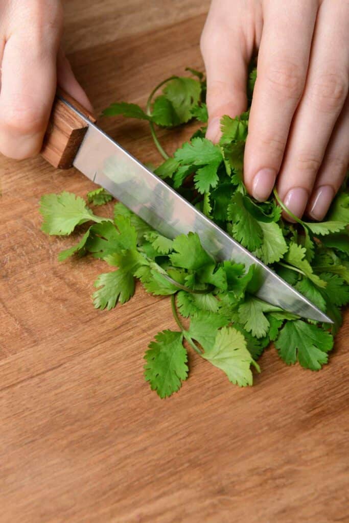 A person slicing cilantro on a wooden cutting board.
