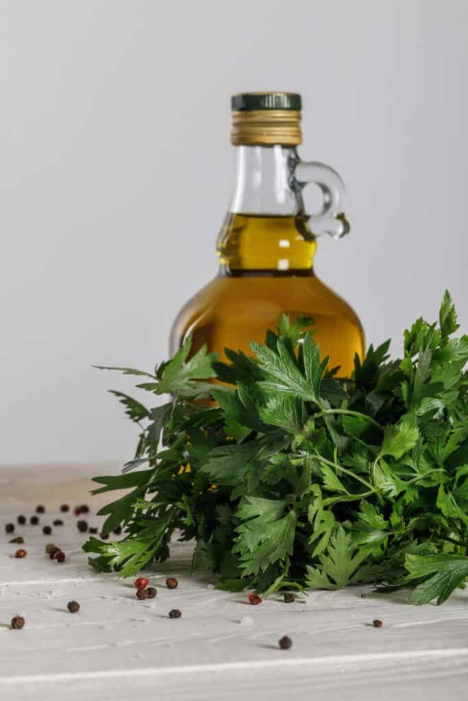 A bottle of olive oil and parsley on a wooden table.