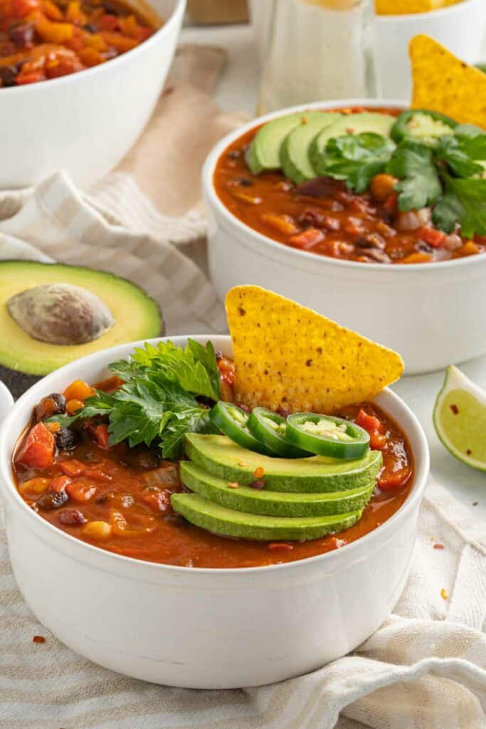 Two bowls of chili with tortilla chips and avocado.