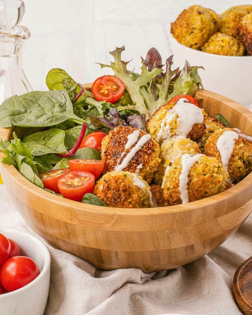 A wooden bowl filled with falafel balls and tomatoes.