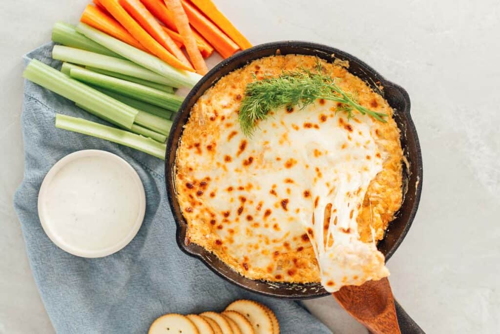 Cheesy Buffalo Jackfruit dip in a skillet with carrots and celery.