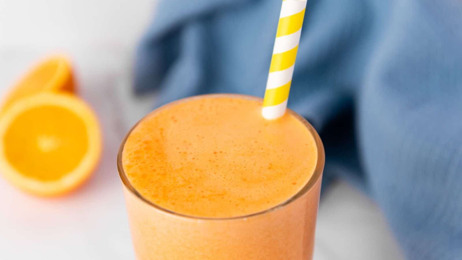 An orange smoothie with a striped straw.