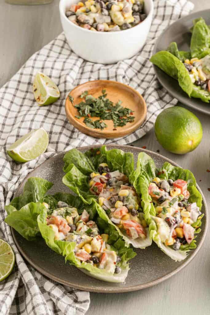 A plate of lettuce wraps with black beans, tomatoes and limes.