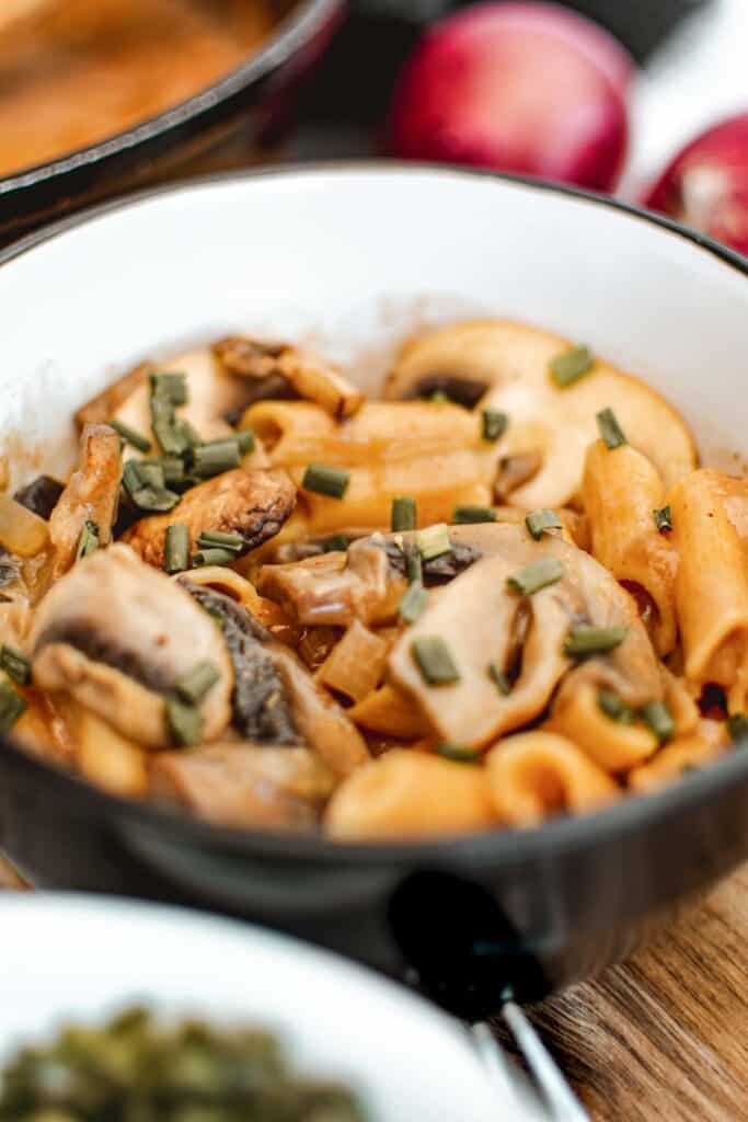 A bowl of pasta with mushrooms and green onions.