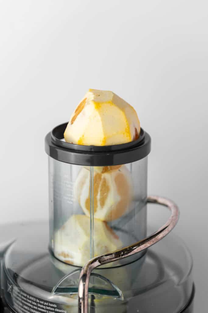 A citrus juicer with peeled oranges and lemon in it.