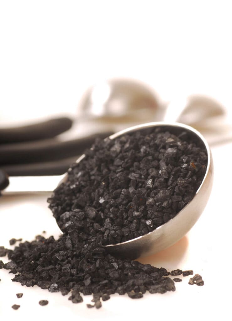 Black sea salt in a spoon on a white surface.