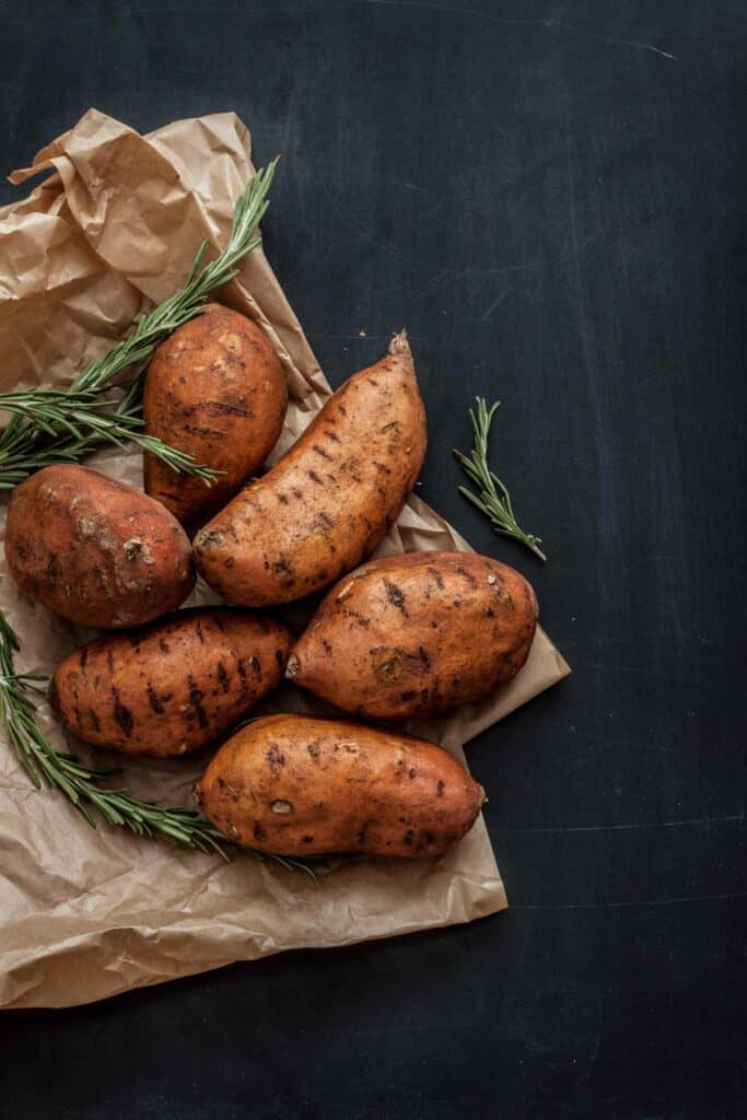 Sweet potatoes in a brown paper bag with rosemary sprigs.