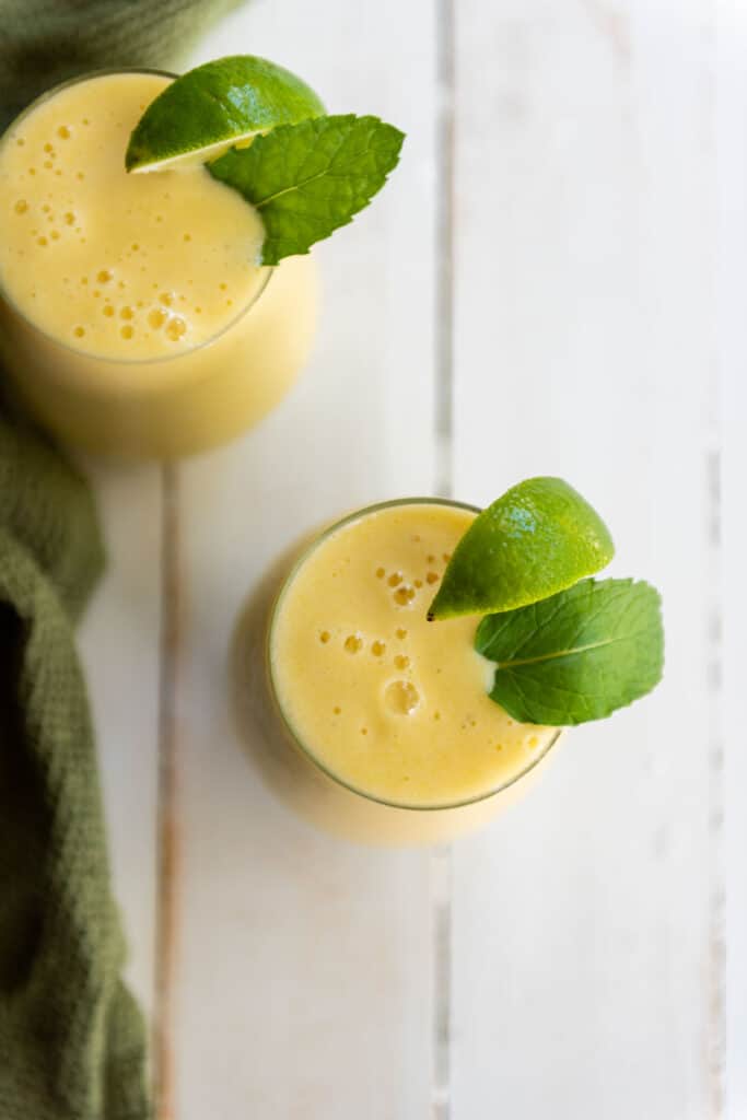 Two glasses of tropical mango smoothie with mint leaves.