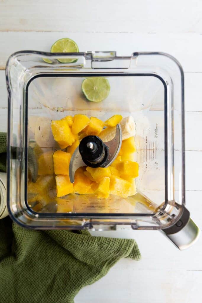 A blender filled with mangoes, bananas, and pineapples.