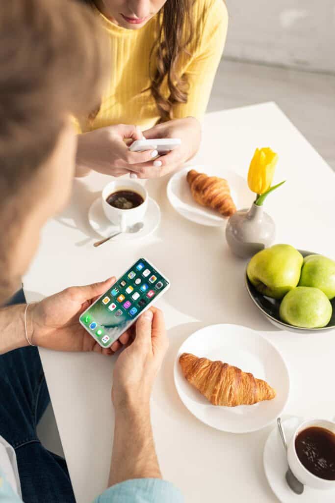 A man and woman sitting at a table with a cell phone and croissants.