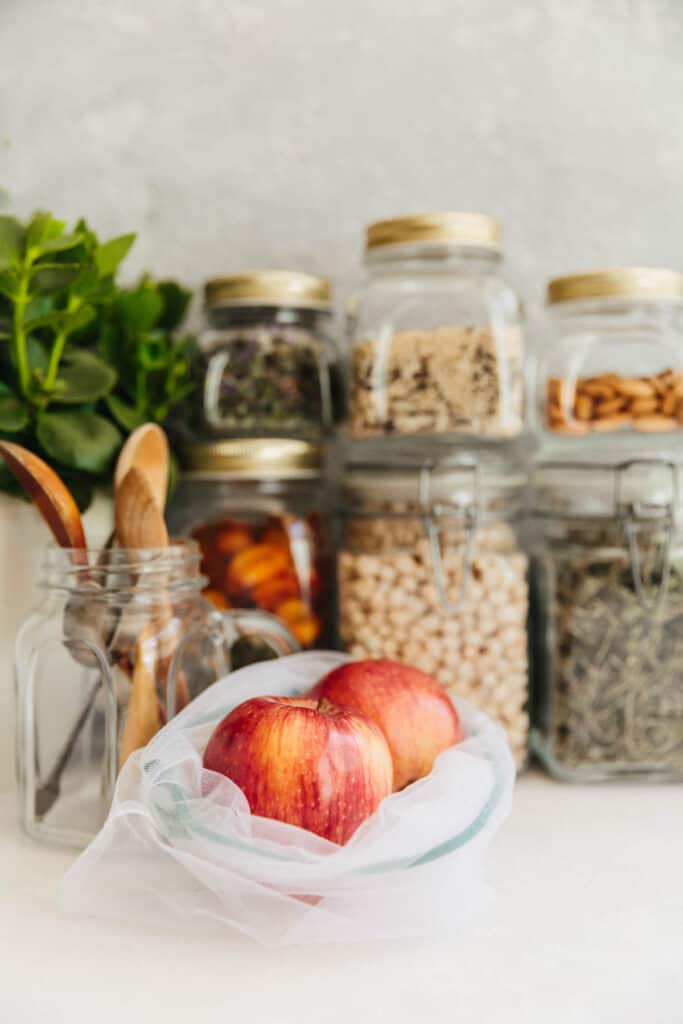 Jars of nuts, seeds and apples on a white table.