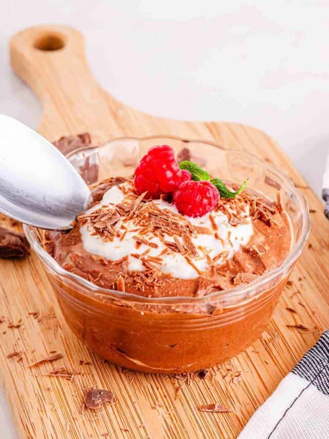 Chocolate mousse in a bowl with whipped cream and raspberries.