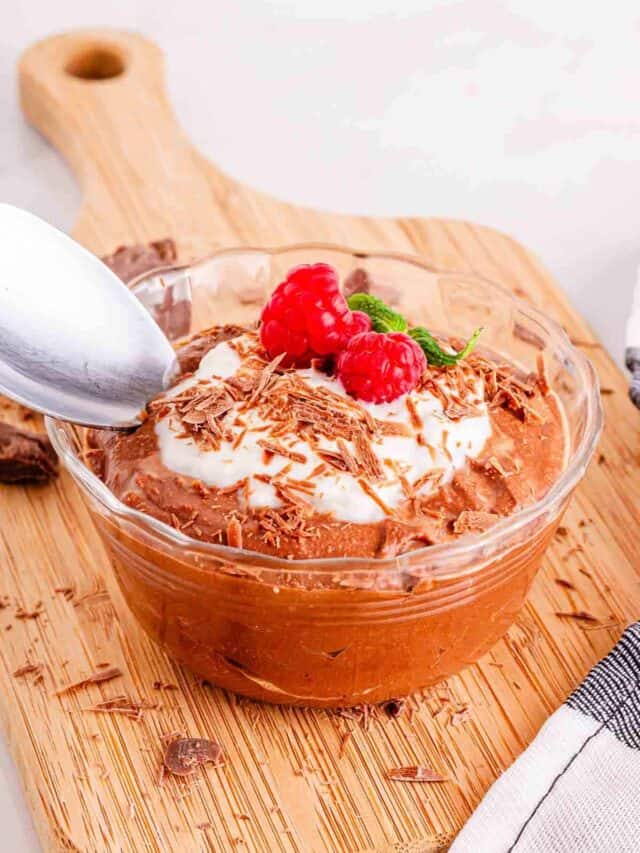 Chocolate mousse in a bowl with whipped cream and raspberries.