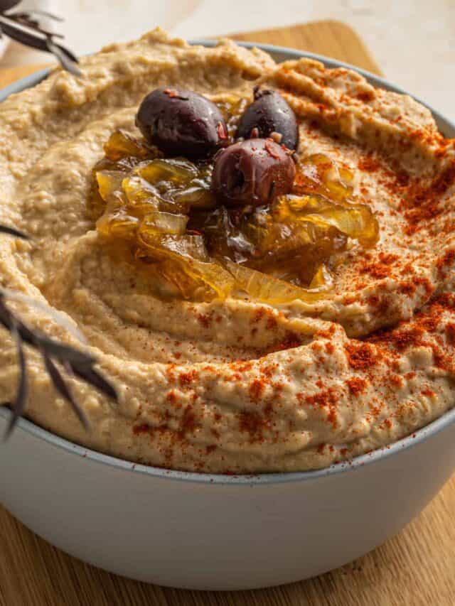 A bowl of hummus with olives and spices.