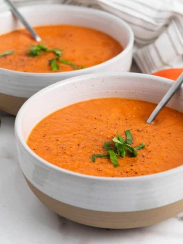 Two bowls of tomato soup with a spoon.