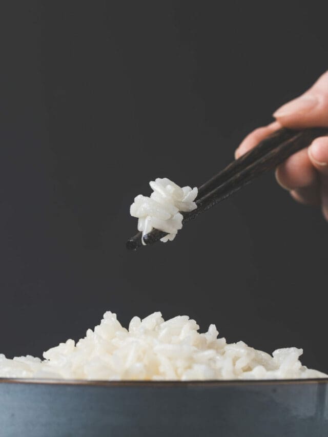 A person holding chopsticks over a bowl of rice.
