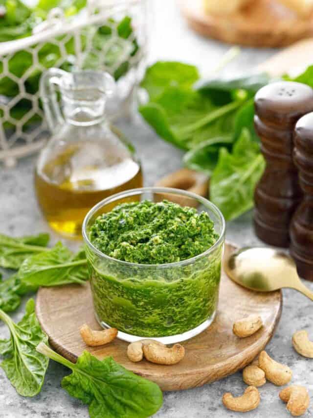A bowl of spinach pesto on a table with cashew nuts.