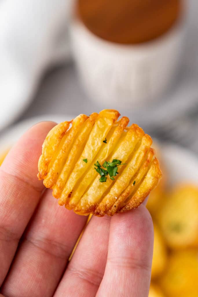 A person holding a small piece of fried potato cooked in an air fryer.