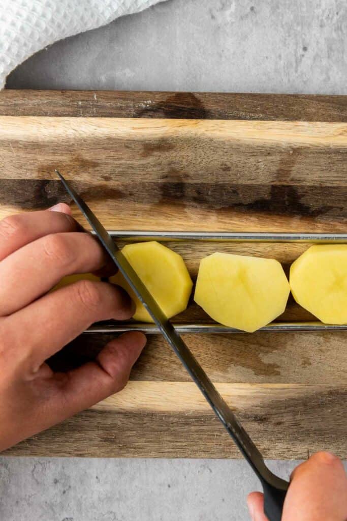 A person cutting potatoes on a cutting board for their air fryer.