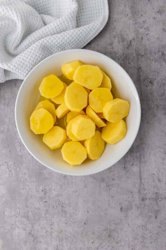 Sliced potatoes in a white bowl on a grey background, perfect for air fryer.