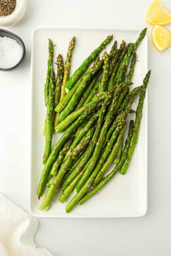 Air fryer asparagus on a white plate with lemon on the side.