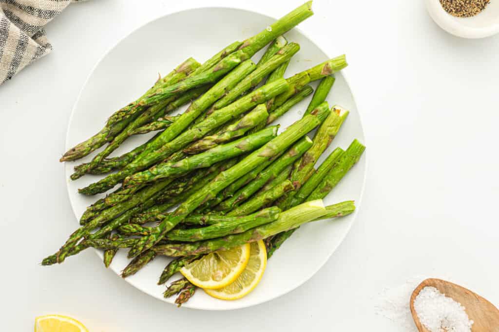 Air fryer asparagus on a white plate with lemon.