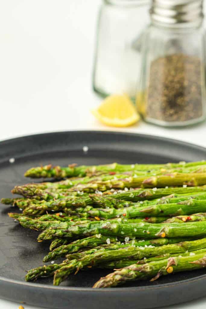 Air fryer asparagus on a black plate with lemon on the side.