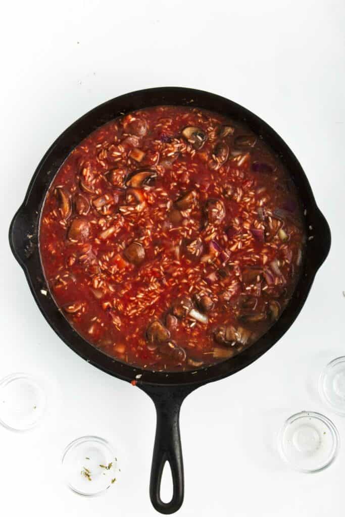 A mixture of Jasmine rice and mushroom with tomato sauce in a skillet.